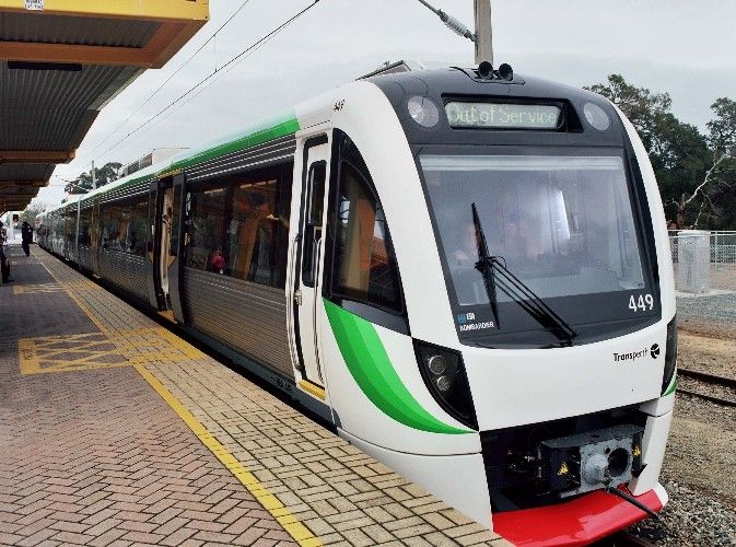 a white and green train pulling into a station next to a platform with people walking on it