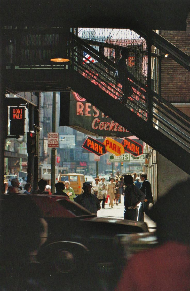 people are walking down the sidewalk under some signs and stairs on a city street at night