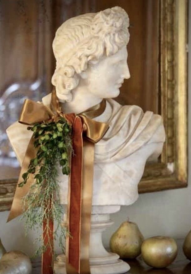 a white busturine with an orange ribbon around it's neck and some pears next to it