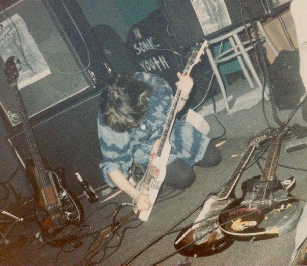 a man sitting on the floor with his guitar in front of him and other musical equipment around him