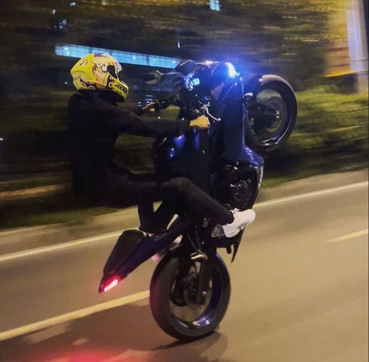 a man riding on the back of a motorcycle down a street at night with its lights on