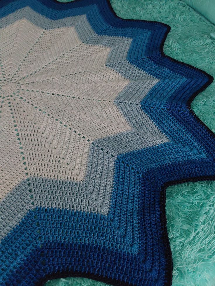 a blue and white crocheted blanket laying on top of a green bed spread