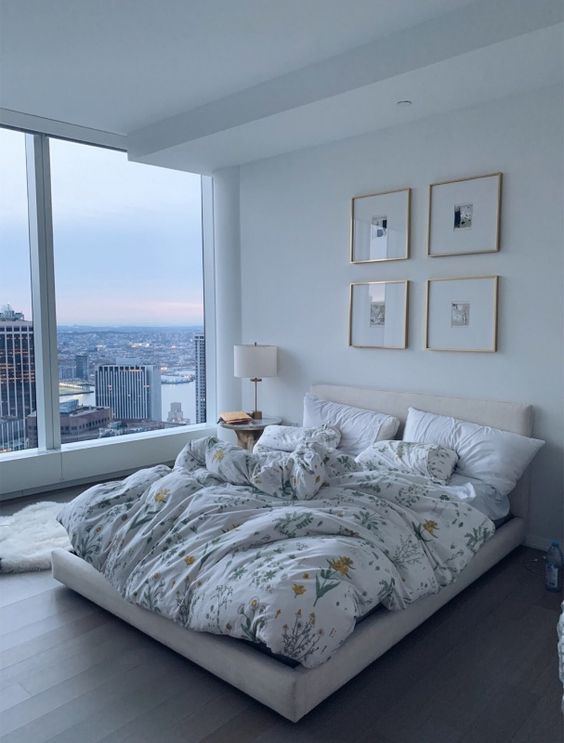 a large bed sitting in the middle of a bedroom next to a window with city view