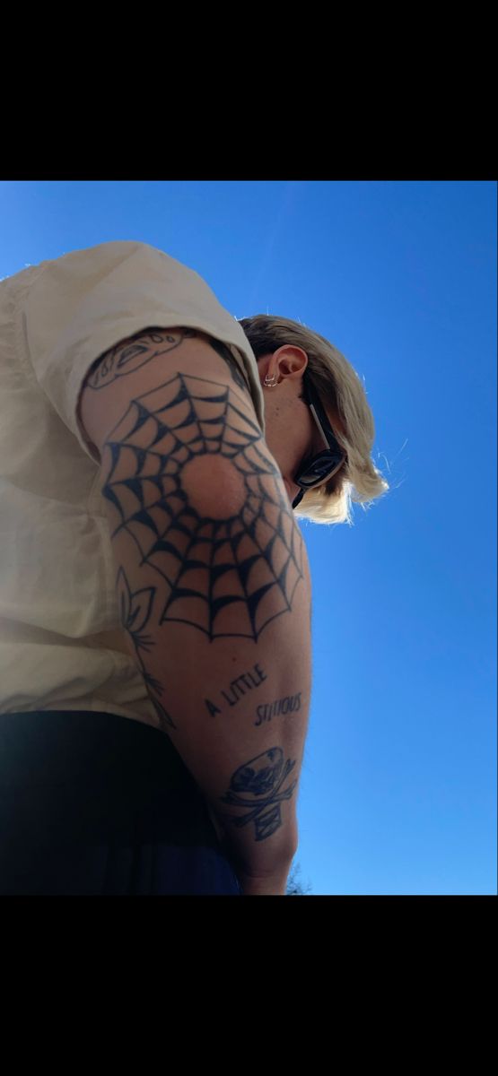 a man with a spider web tattoo on his arm and shoulder is looking up at the sky