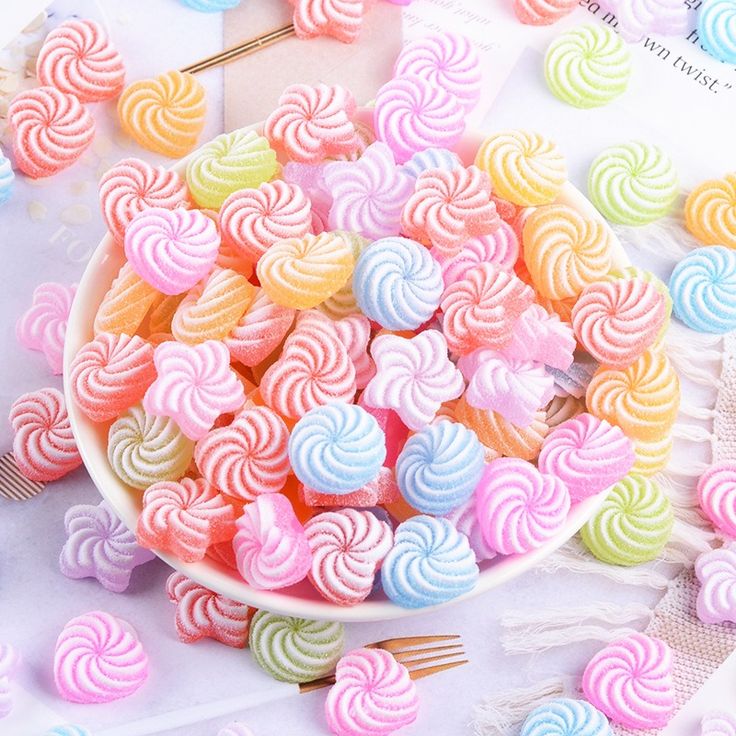 a bowl filled with rainbow lollipops on top of a table next to other candies