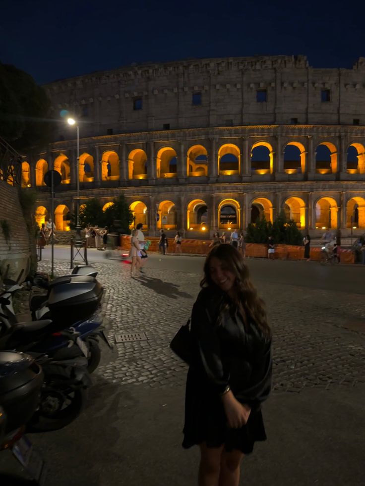 a woman standing in front of an old building at night with lights on the windows