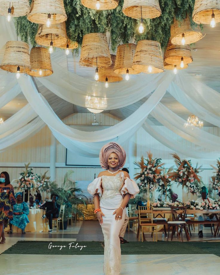 a woman in a white dress and head scarf standing on a stage with lights hanging from the ceiling