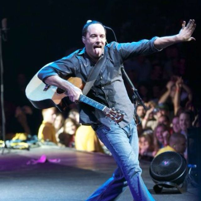 a man holding a guitar while standing on top of a stage with his arms outstretched