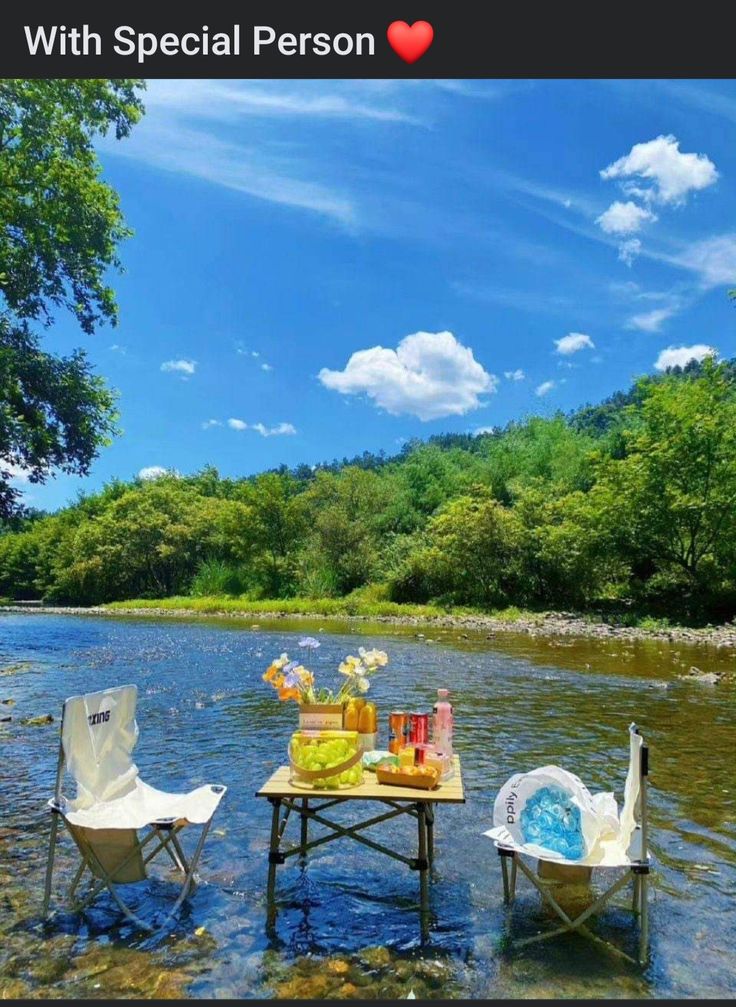 two lawn chairs sitting on top of a river next to a table with food and drinks