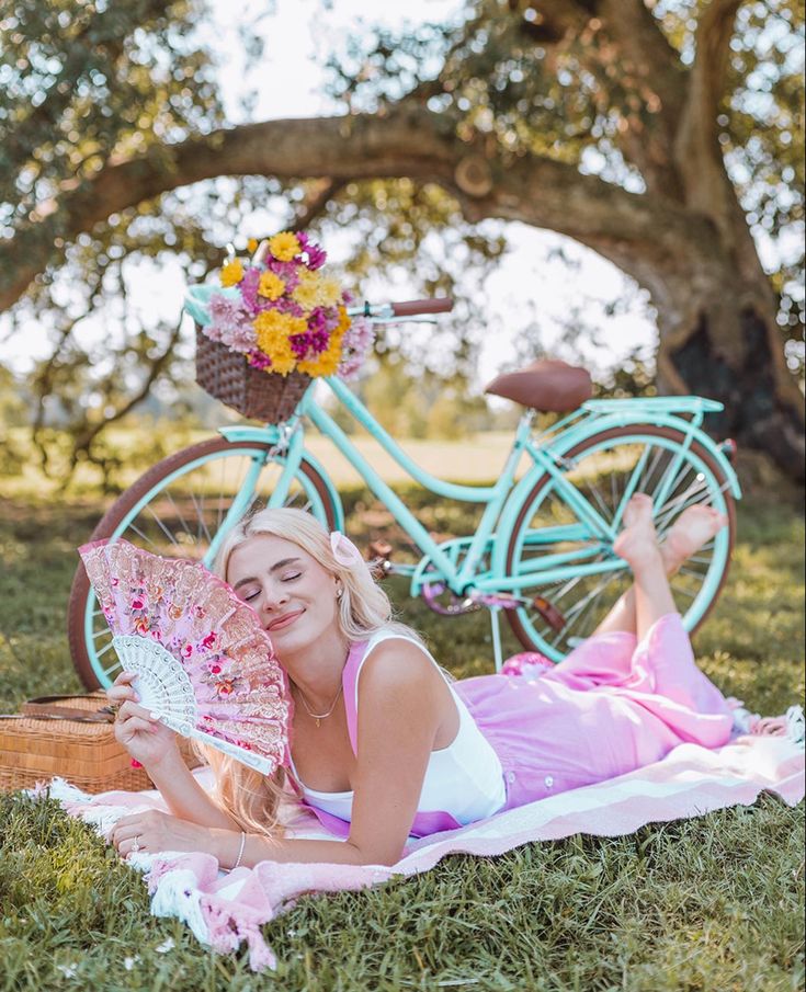 a woman laying in the grass with a pink and white umbrella next to a bicycle