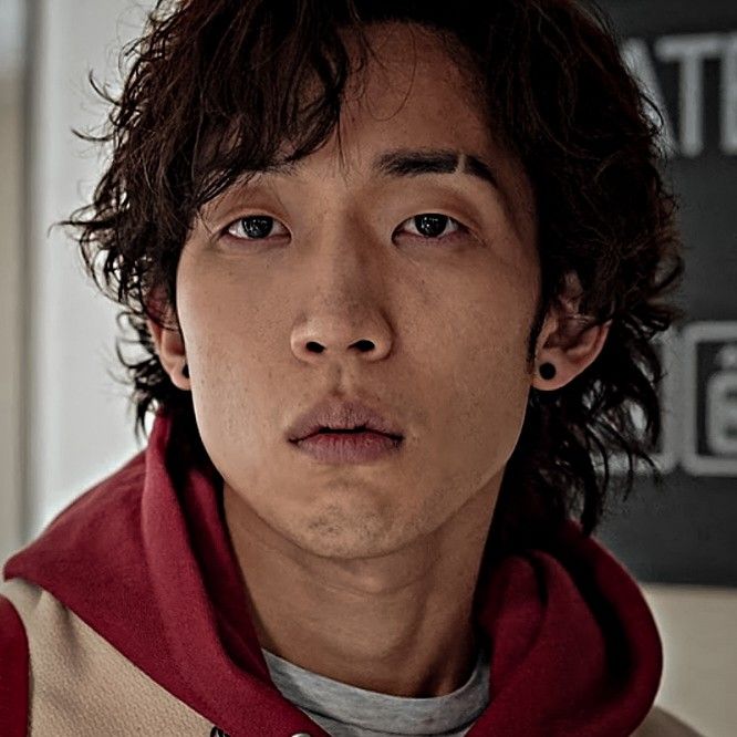 a young man with long hair wearing a red and tan hoodie looking at the camera