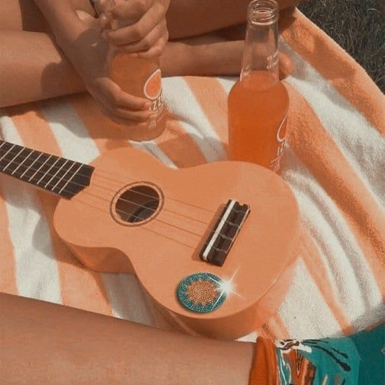 a person sitting on a towel with a ukulele and two bottles of orange juice