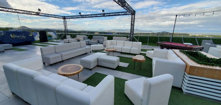 an outdoor seating area with white couches and tables on top of grass covered ground