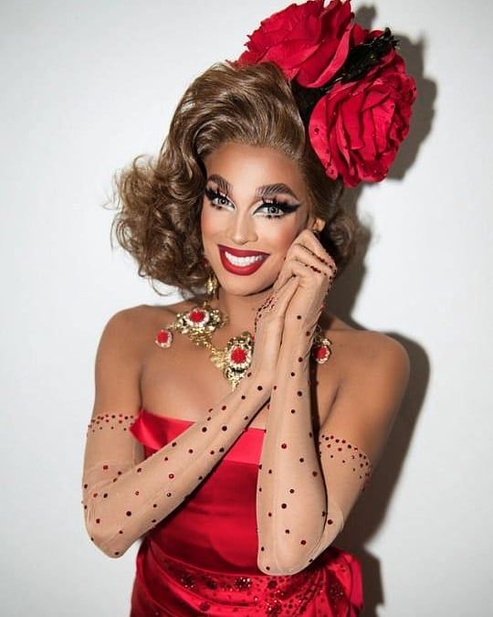 a woman in a red dress is posing with her hands on her face and holding a flower