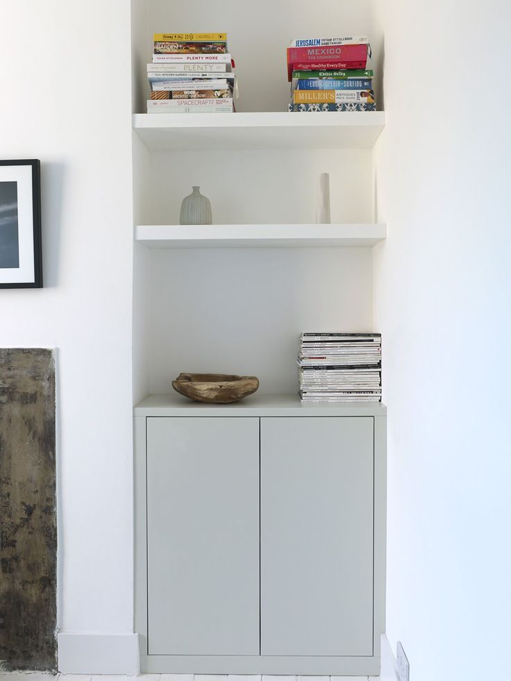 a white shelf with books on top of it next to a wall mounted clock and pictures