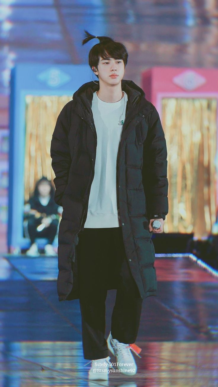 a male in a black jacket and white shirt is walking down the runway with his hands in his pockets