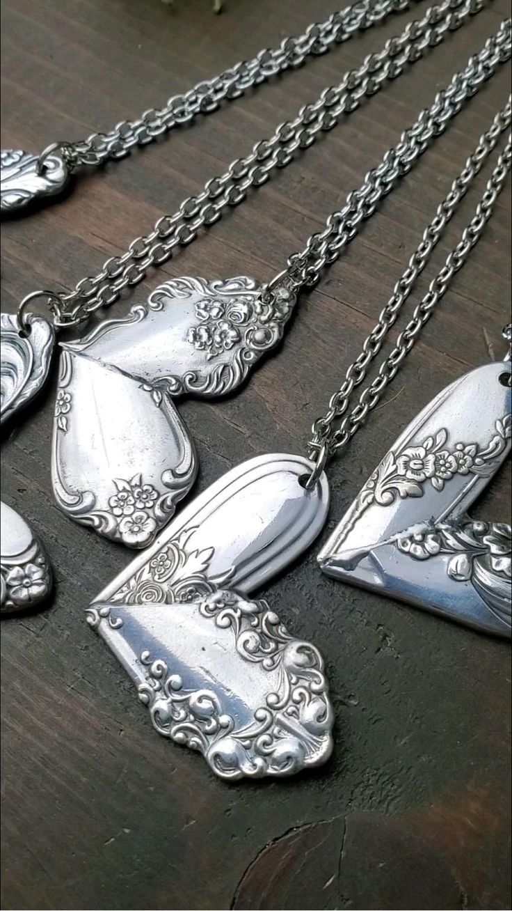 several silver necklaces on a wooden table with flowers in the middle and one is hanging from