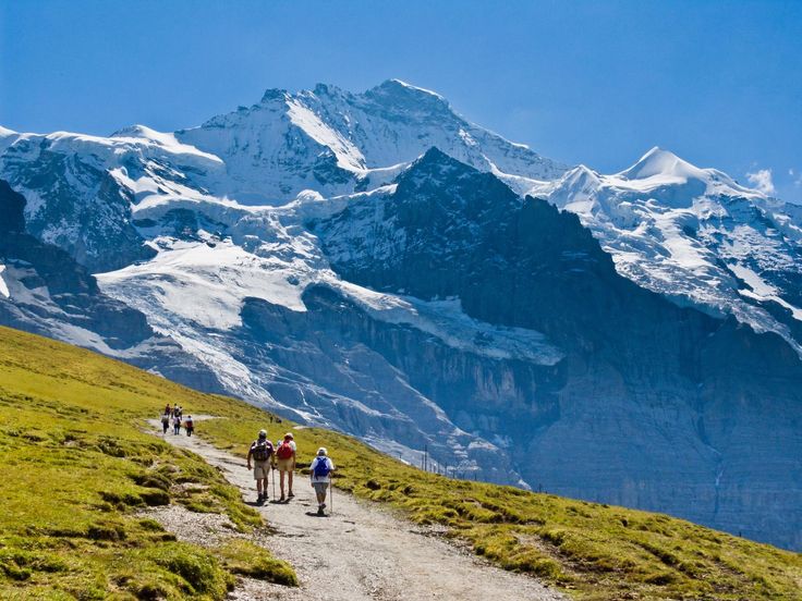 some people are walking up a trail with mountains in the backgrouds and snow on them