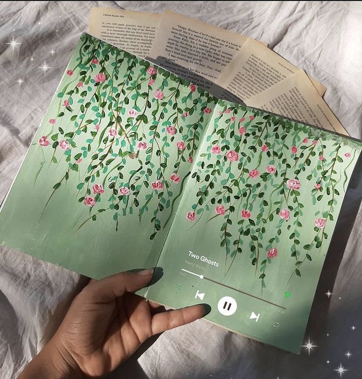 an open book with pink flowers and green leaves on it, held in someone's hand