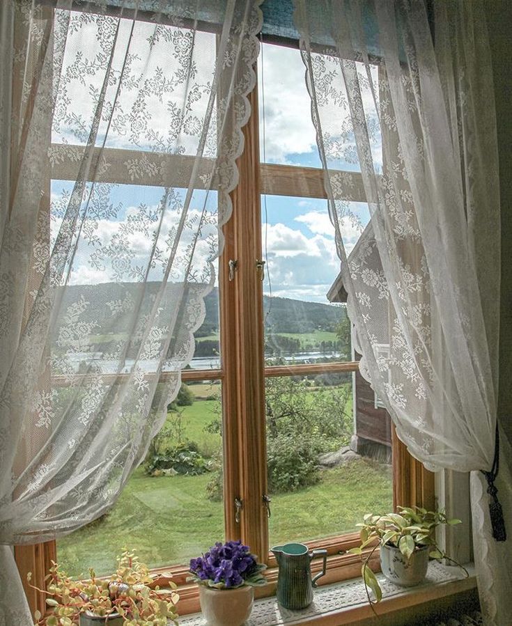 there is a window with sheer curtains and flowers in the vases on the windowsill