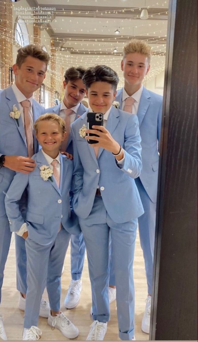 a group of young men in blue suits taking a selfie with a cell phone