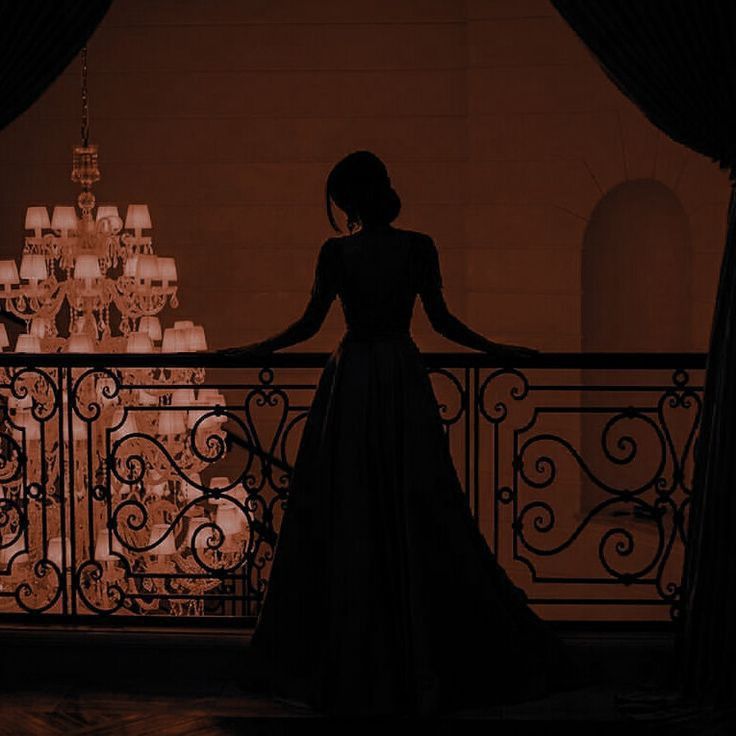 a woman standing on a balcony next to a chandelier with candles in the background