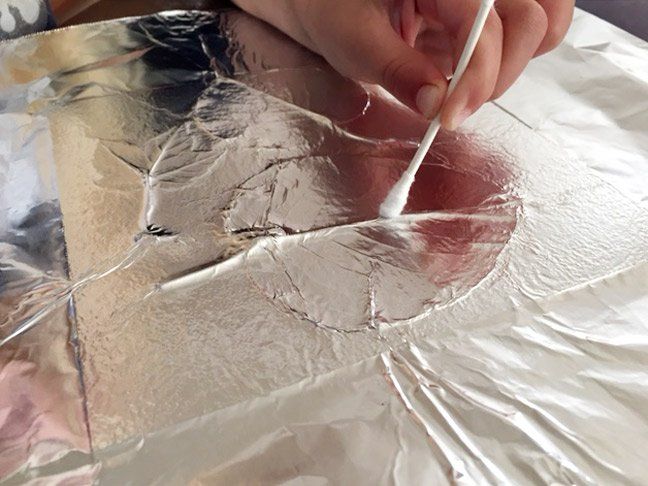 a person is holding a toothbrush in their hand and painting on tin foil with silver flakes