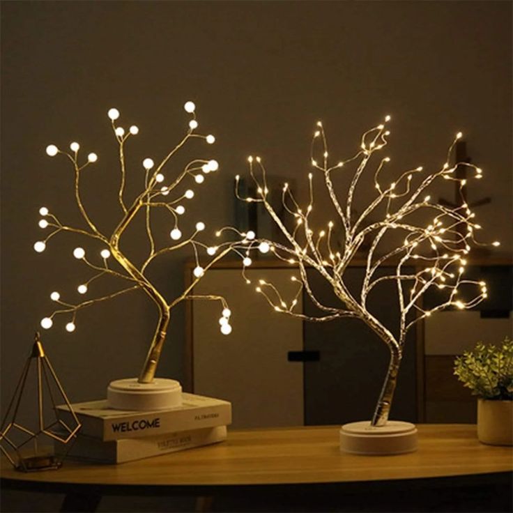 a lighted tree is sitting on top of a table next to a potted plant