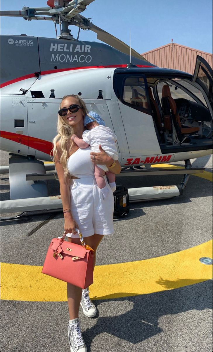 a woman holding a baby standing in front of a helicopter with her hand on her chest