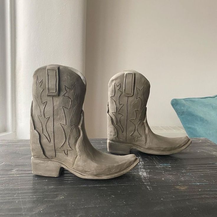 a pair of gray cowboy boots sitting on top of a wooden table