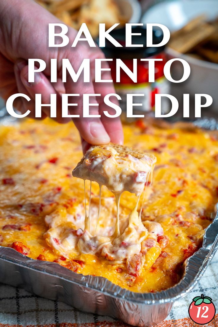 a hand holding a piece of baked pimentoo cheese dip over a casserole dish