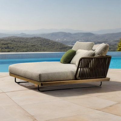 an outdoor chaise lounge next to a swimming pool with mountains in the back ground