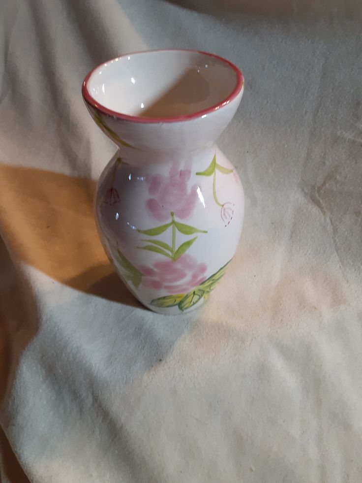 a small white vase sitting on top of a table next to a cloth covered floor