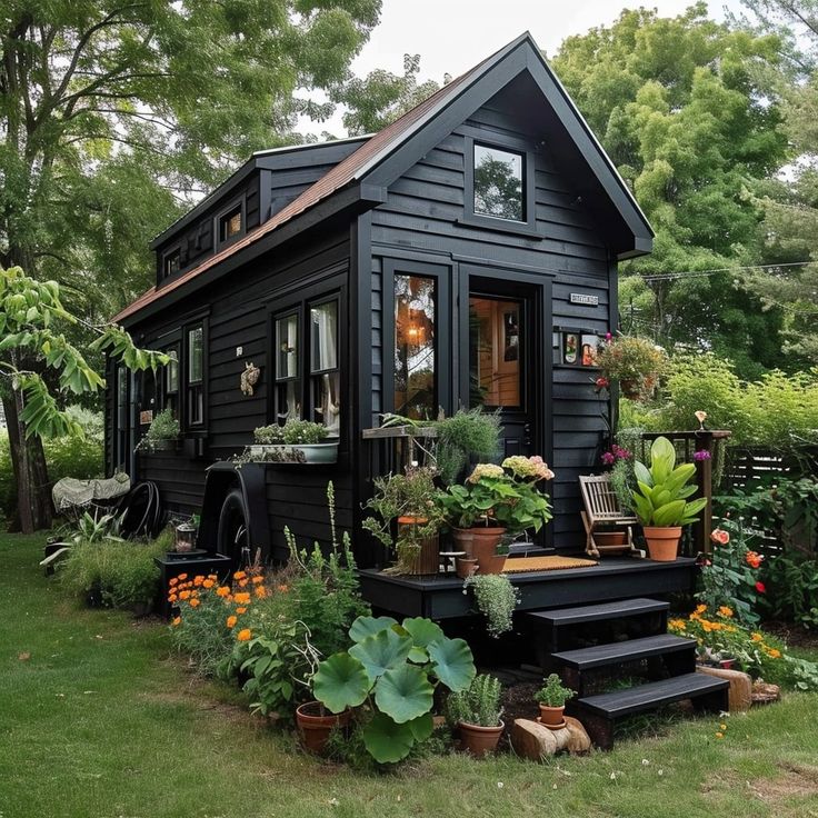 a black tiny house surrounded by plants and flowers