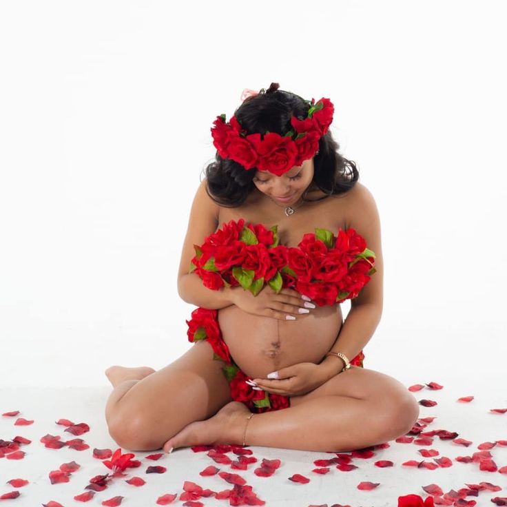 a pregnant woman sitting on the floor surrounded by rose petals with her hands in her stomach