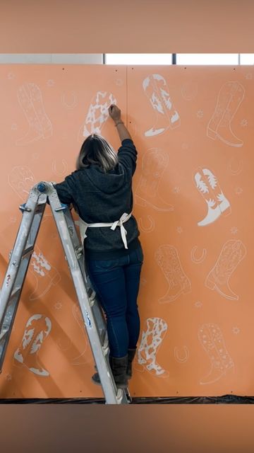 a woman standing on top of a step ladder painting a wall with cartoon drawings all over it