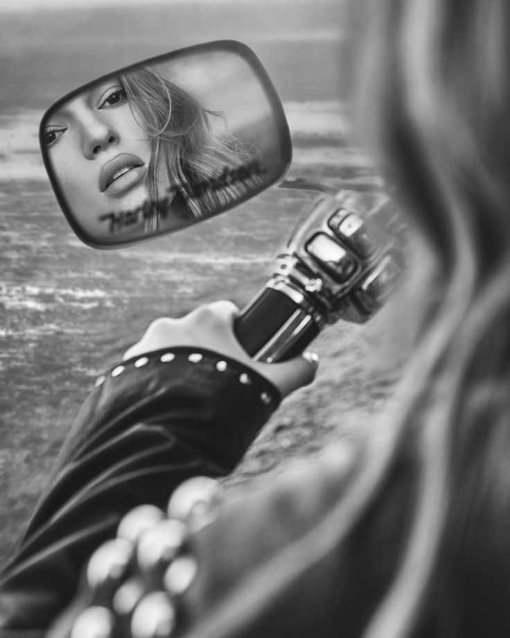 a woman taking a selfie in the side mirror of a car with her reflection