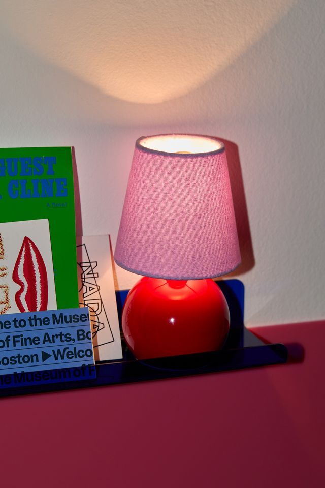 a red lamp sitting on top of a table next to a book and a pink shade