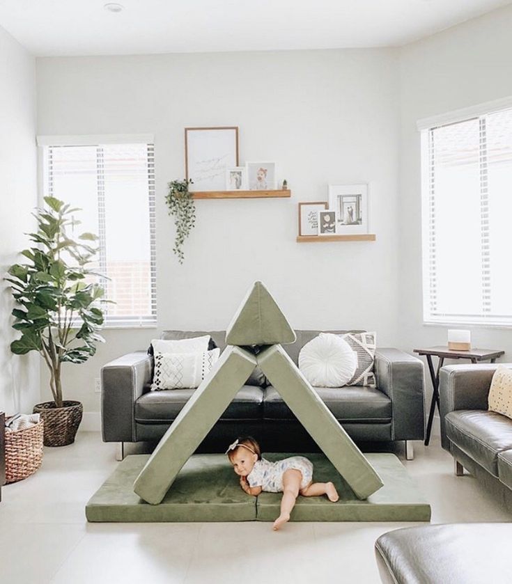 a baby is laying on the floor in front of a fake house shaped like a triangle