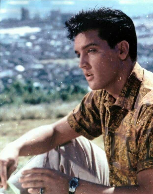 a young man sitting on top of a hill next to a cityscape in the background