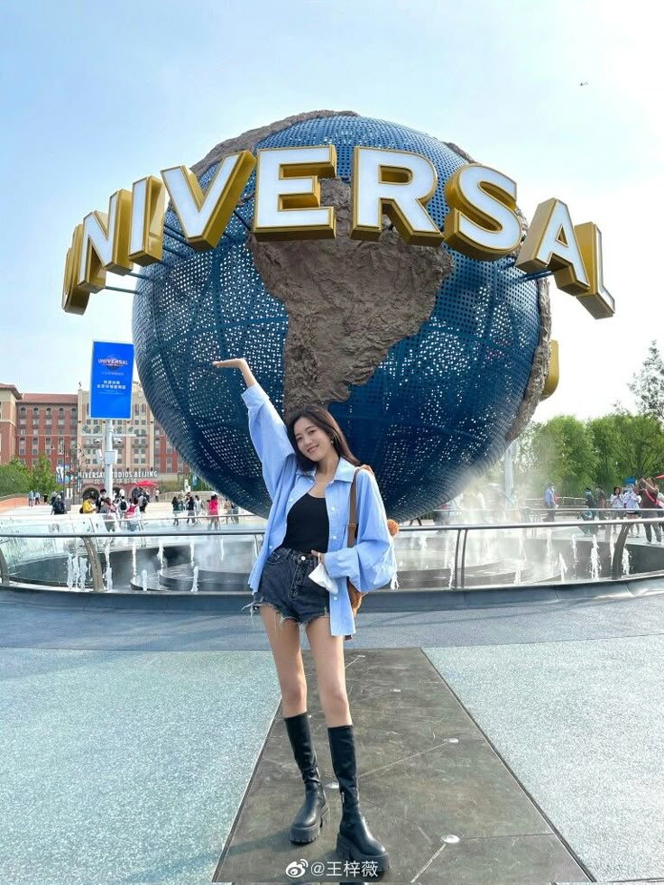 a woman standing in front of the entrance to universal studios with her arms up and one hand raised