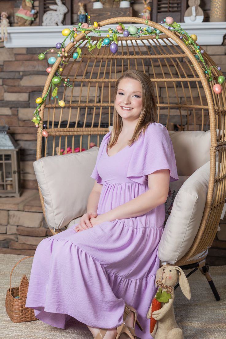 a woman in a purple dress sitting on a wicker chair next to a stuffed animal