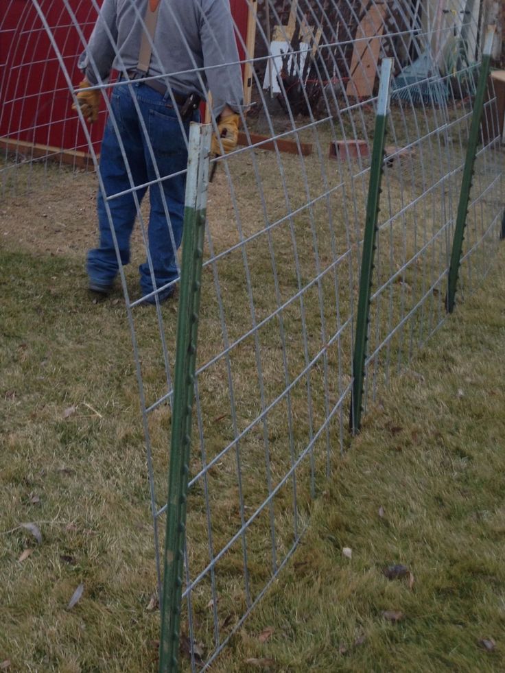 a man standing next to a wire fence on top of a grass covered field in front of a red building