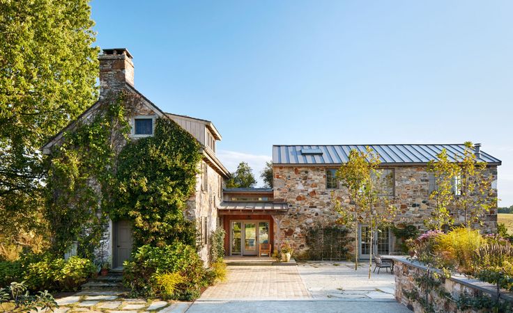 an old stone house is surrounded by greenery and brick walkway leading to the front door