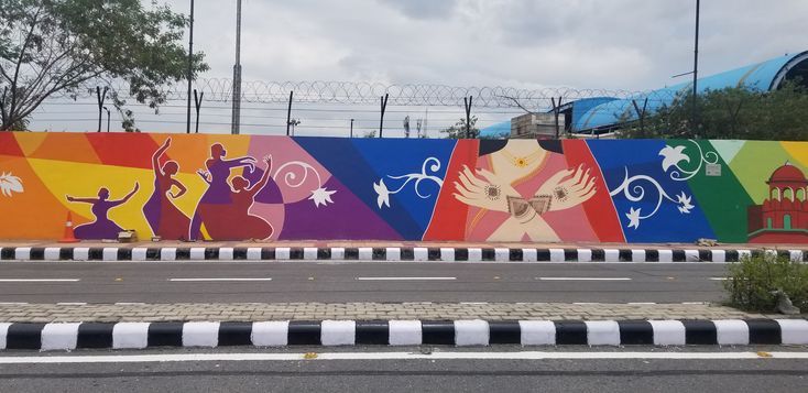 a large colorful wall with people painted on it's sides next to a street