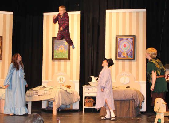 people are standing on stage in front of paintings and other items, with one person jumping up into the air