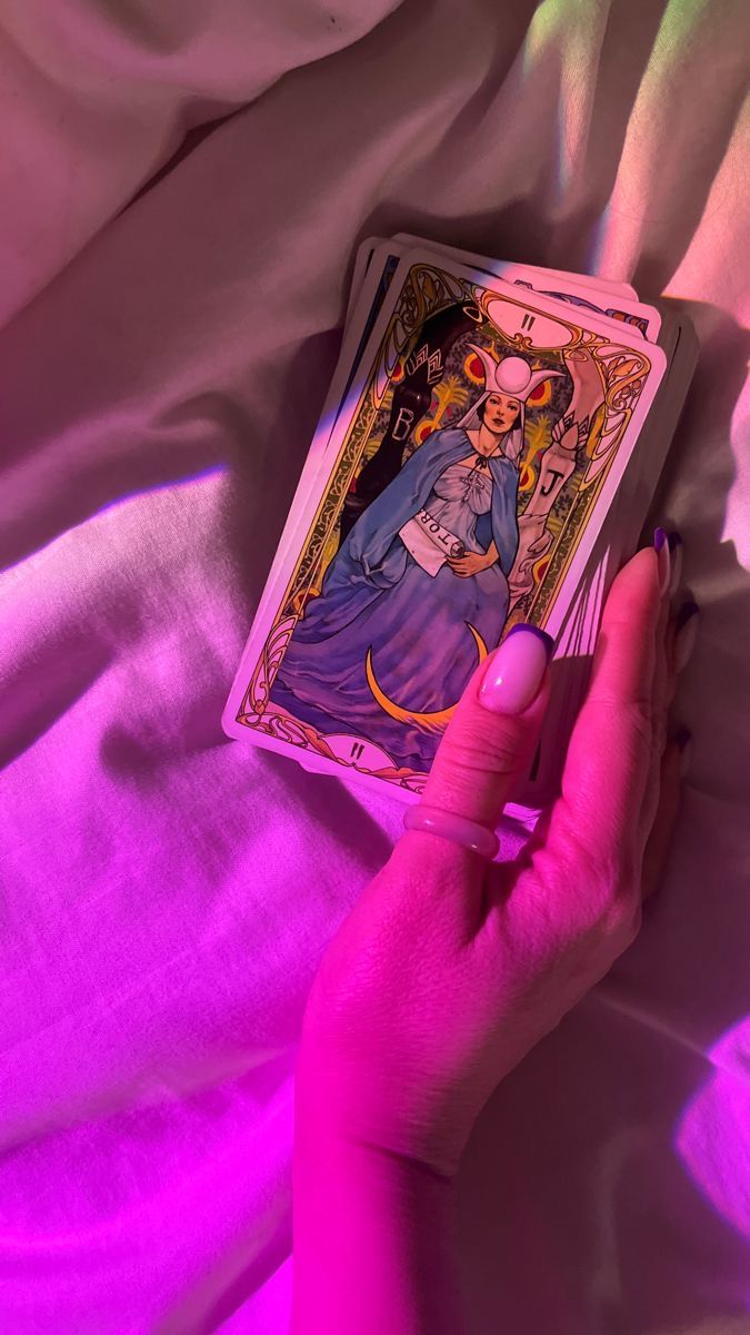 a person holding up a tarot card in their hand on a bed with pink sheets