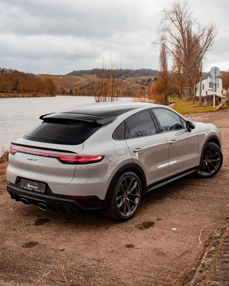 the rear end of a silver porsche suv parked in front of a body of water