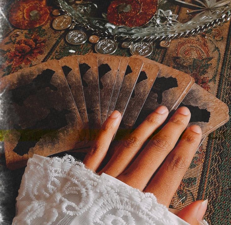 a woman's hands holding four playing cards on top of a table with other items