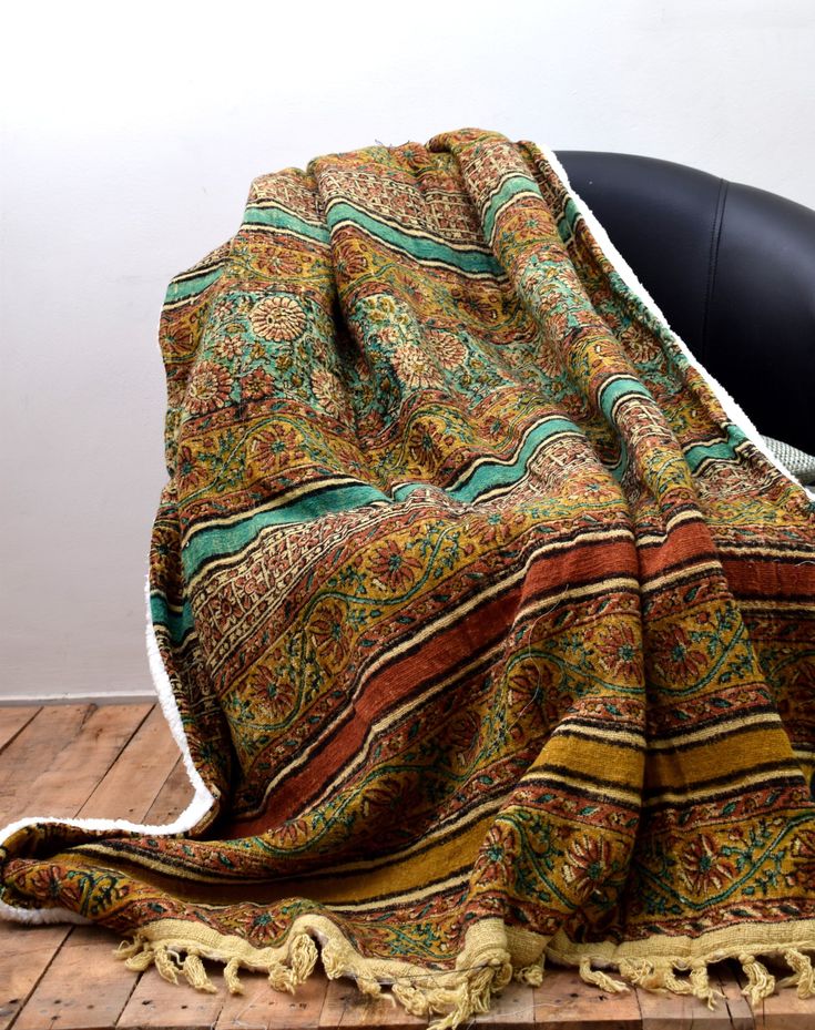 a blanket sitting on top of a wooden floor next to a black chair and white wall